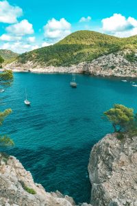 Sailboats drift in a stunning turquoise bay surrounded by rocky cliffs in Ibiza, Spain.