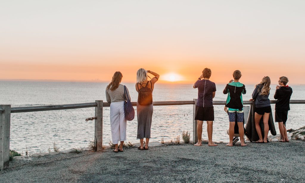 A group of people watching a beautiful sunset over the ocean, their backs to the camera.